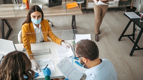 Face-masked woman helps patients complete paperwork