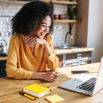 A woman at her counter smiling at a laptop, showcasing a side hustle job in her spare time.