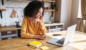 A woman at her counter smiling at a laptop, showcasing a side hustle job in her spare time.