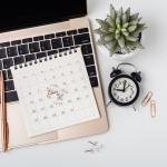 An aerial view of a computer calendar, pen, plant, and time clock to represent time blocking.