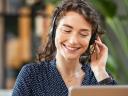A woman wears a headset and works at a laptop, possibly impacting contact centre revenue.