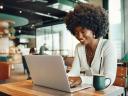 A smiling young Black woman uses her laptop to get self-service customer service in a cafe