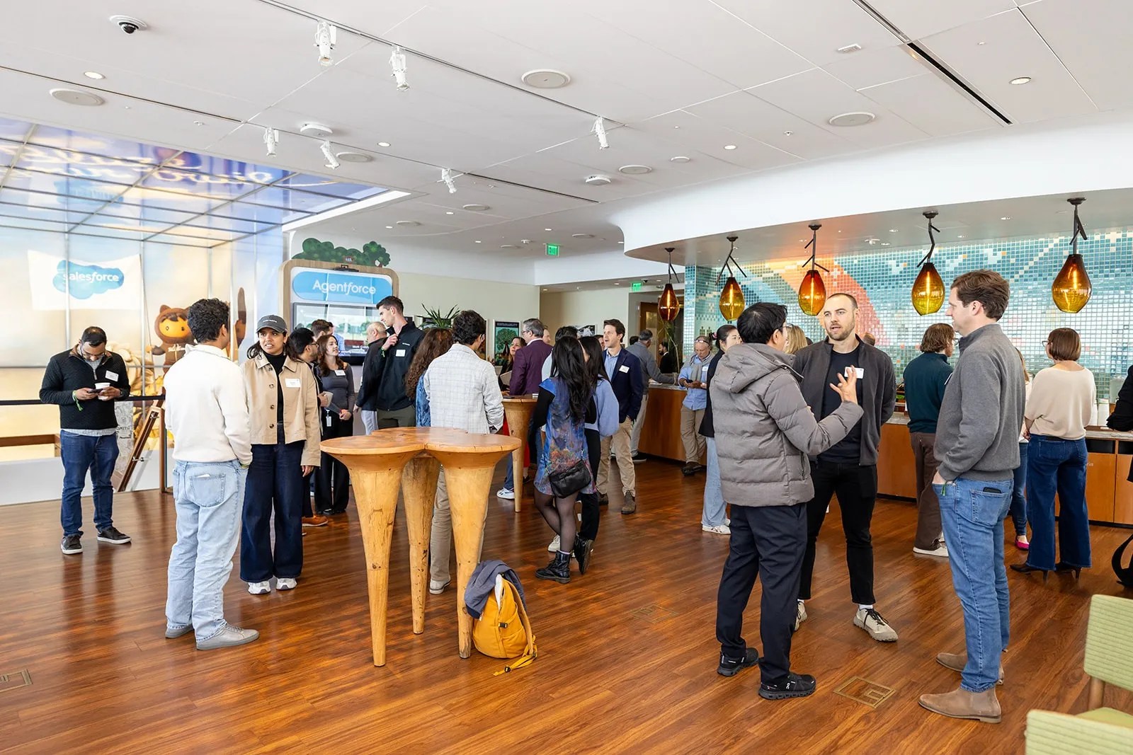 A crowd of people gathering and networking in a modern Salesforce event venue with wood floors.