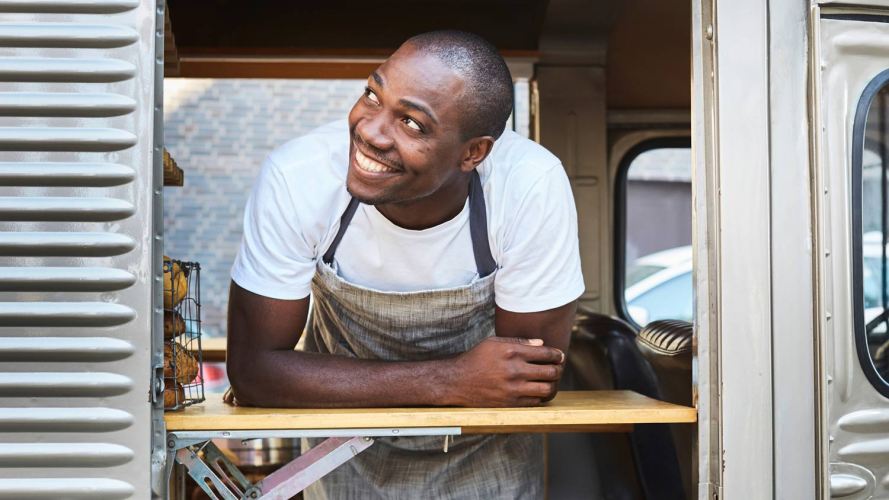 smiling worker in an apron looking out the window of a food truck
