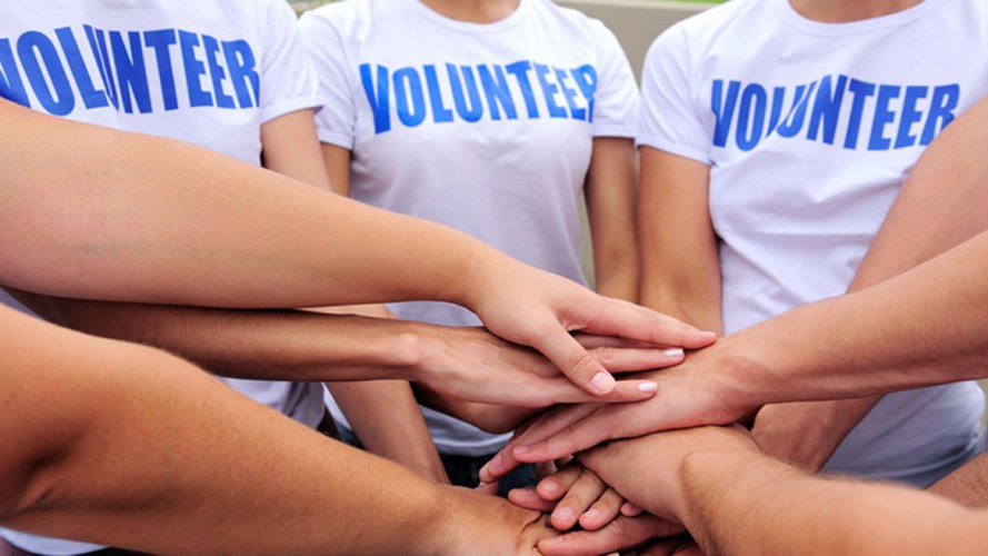 A group of multiple people wearing a "Volunteer" shirt and joining hands in a huddle
