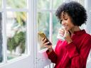 Woman in a red shirt checks her phone inside on a rainy day while holding a white coffee mug / email deliverability