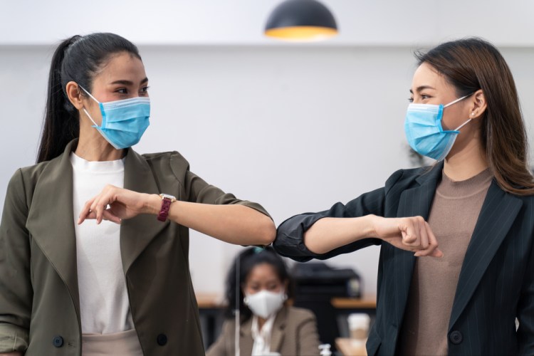 two office workers in masks giving each other an elbow bump