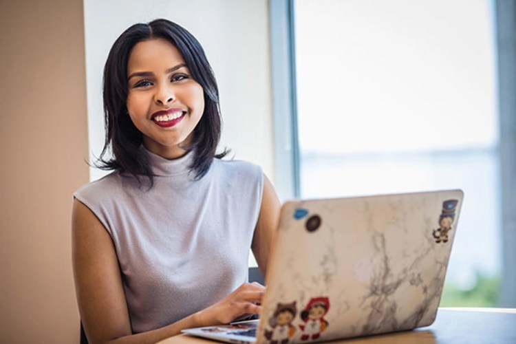 A Salesforce employee sitting next to her laptop, smiling at the camera.