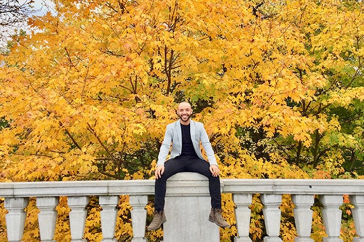 Johnny sitting on the edge of a structure with yellow-leafed trees in the background.