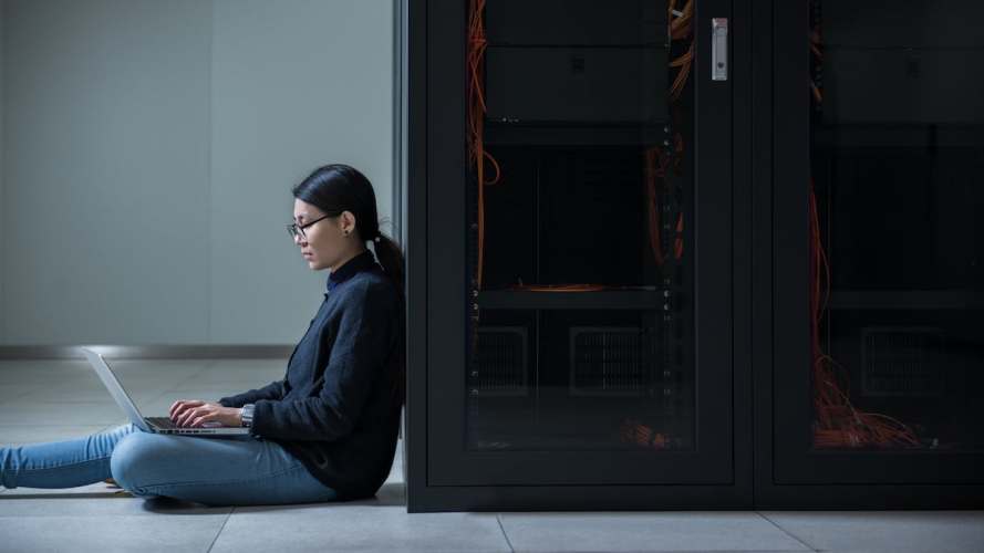 Woman working beside computer servers. Communications service providers.
