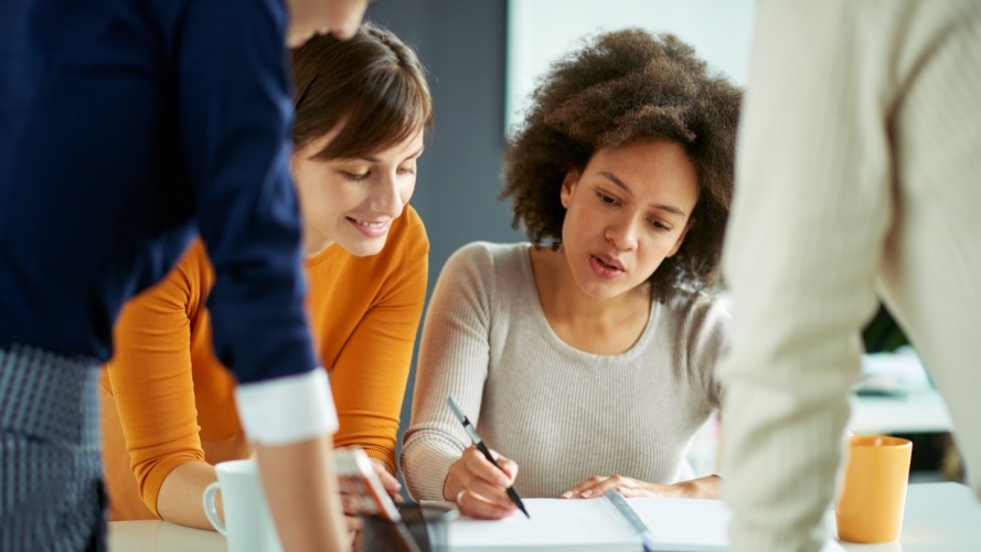 A group of four people collaborate on relationship design viewing a spiral notebook.