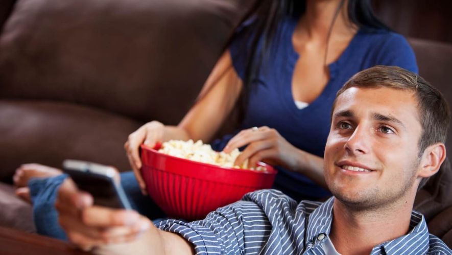 man and a woman watching TV and eating popcorn