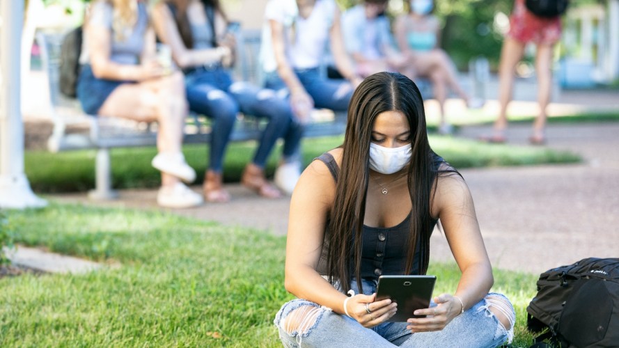 Woman wearing face mask sits on campus green