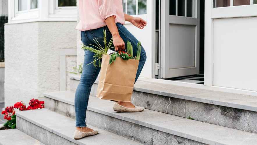 Woman walking a bag of groceries into her home