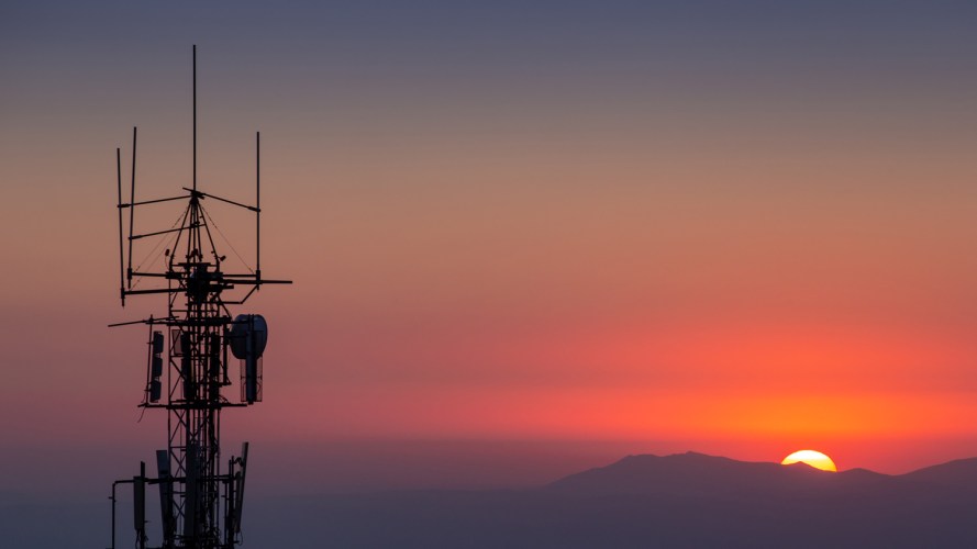 the sun at the horizon behind a telecommunications tower