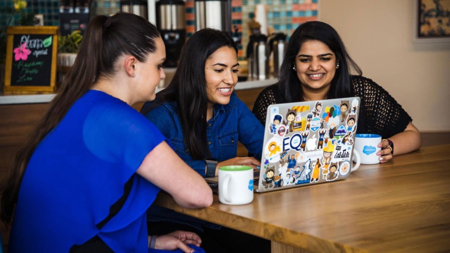 Female Salesforce colleagues gather around a laptop