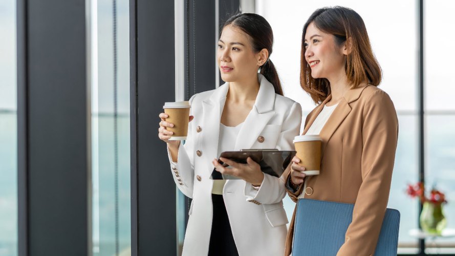 Two women of Asian descent look our a window while holding coffee cups: asian american contributions