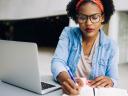 Black woman makes notes on paper while sitting in front of a laptop: small business pandemic entrepreneur