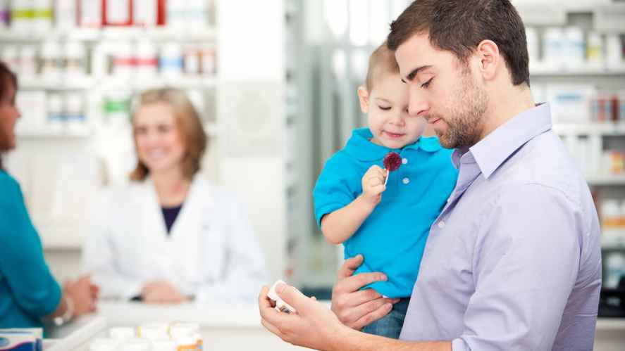Father holding his son while shopping on his phone in a pharmacy