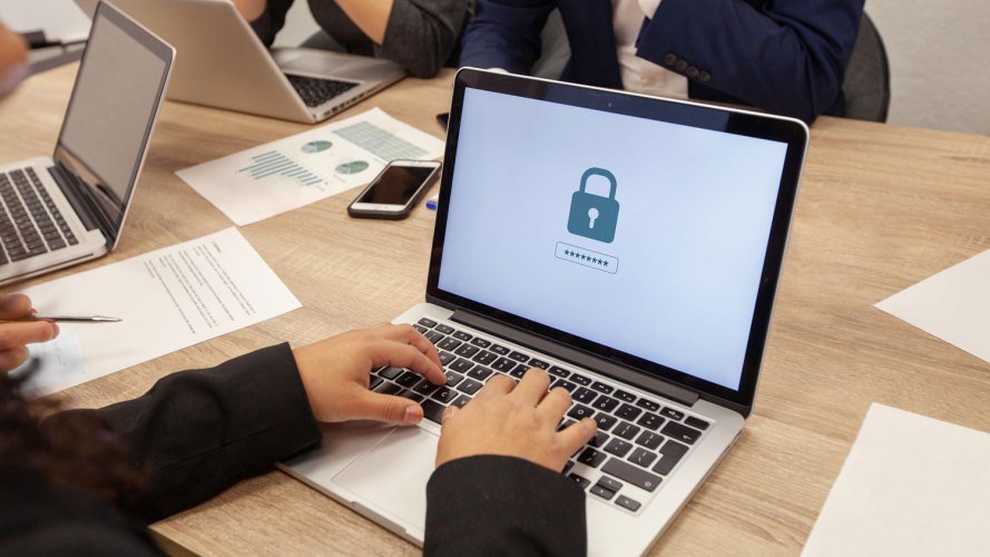 laptops on a table with hands, the screen of the laptop has an image of a lock on it indicating avoiding cybersecurity attacks