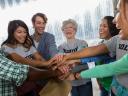 A group of seven people gathering in a huddle and putting their hands together to celebrate a game plan