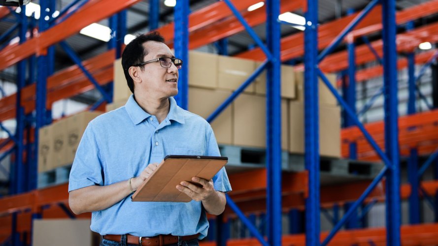 man in a logistics warehouse with boxes on warehouse shelves surrounding him: small business navigate supply chain