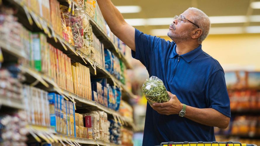 A man shopping at a grocery store reaches for an item on the top shelf: trade promotion management