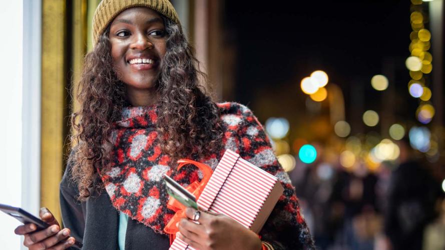 A woman holds a credit card, a phone and a holiday gift box, perhaps a sign of ecommerce success.