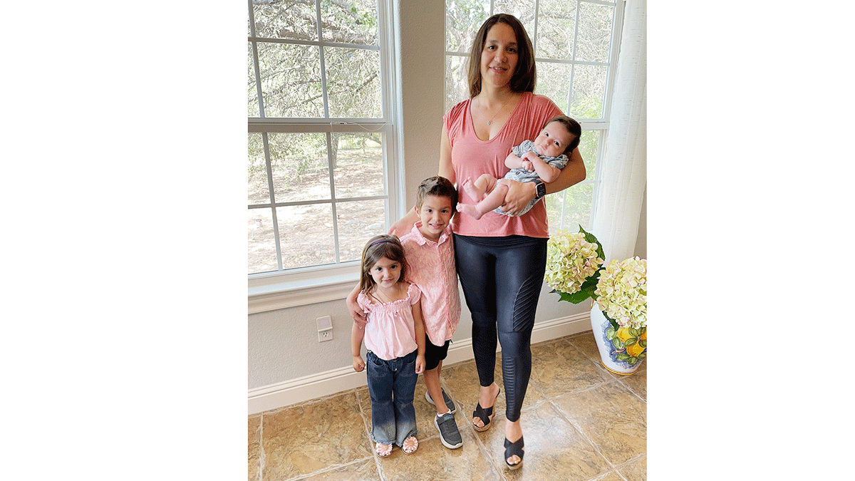 A woman is holding a baby and stands next to two children.