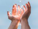Image of two hands holding a string of white lights to symbolize embrace of an idea
