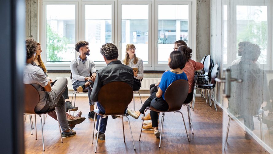 A photo of eight (8) people sitting in a circle in an empty room: employee engagement