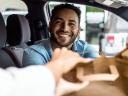 smiling car driver hands a brown bag through passenger side: small business customer experience