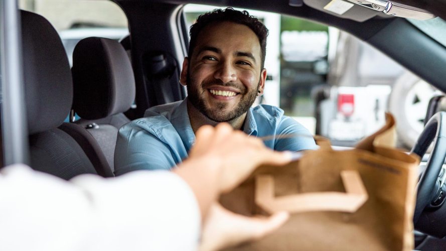 smiling car driver hands a brown bag through passenger side: small business customer experience
