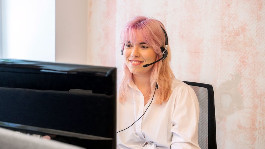 Pink-haired woman with headset on looking at computer screen: customer service in banking, customer experience