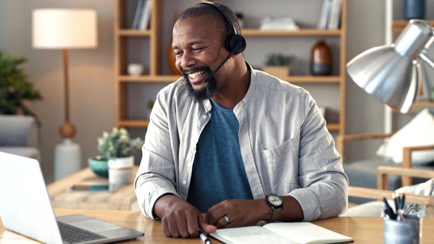 Sales rep smiling while wearing a headset and looking at his laptop: pessimism in sales