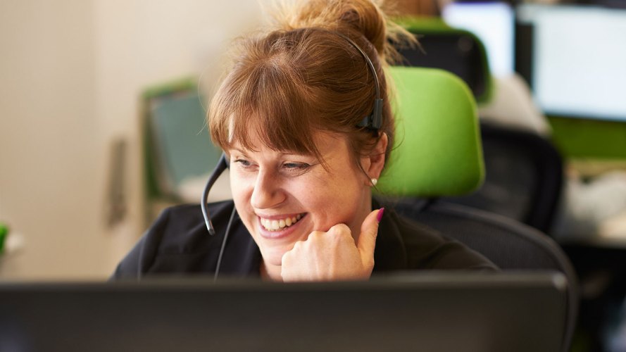 woman wearing headset smiling, looking at her computer screen: contact center burnout