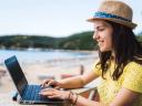 Photo of a woman sitting near a beach, working on her laptop / Marketing Cloud