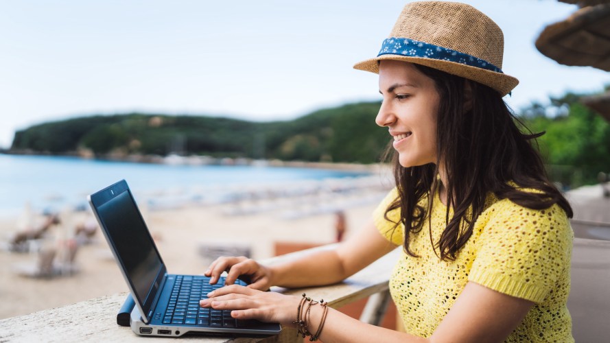 Photo of a woman sitting near a beach, working on her laptop / Marketing Cloud