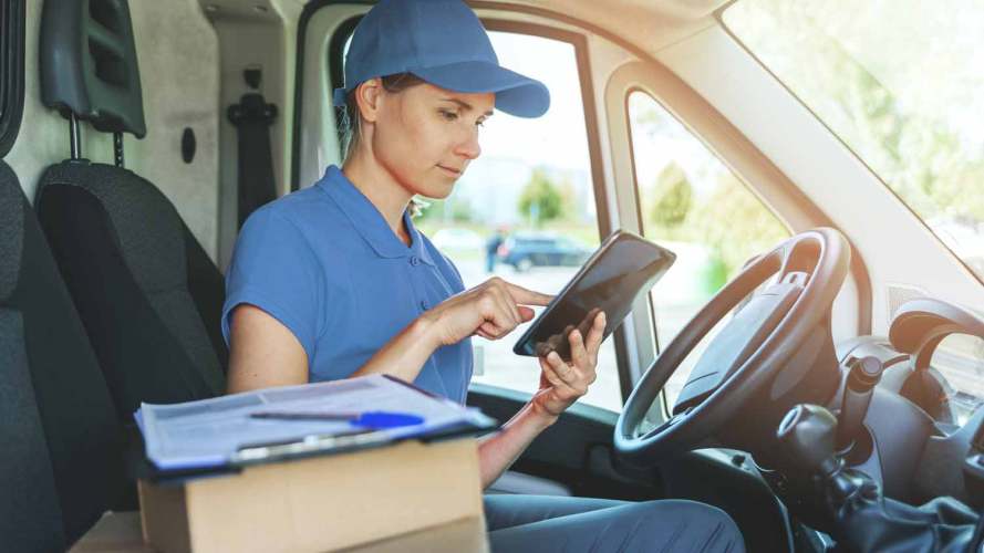 A delivery driver sits behind a steering wheel viewing a tablet: field service agility