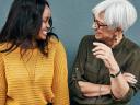 Two female coworkers from different generations chat, part of an intergenerational workforce.