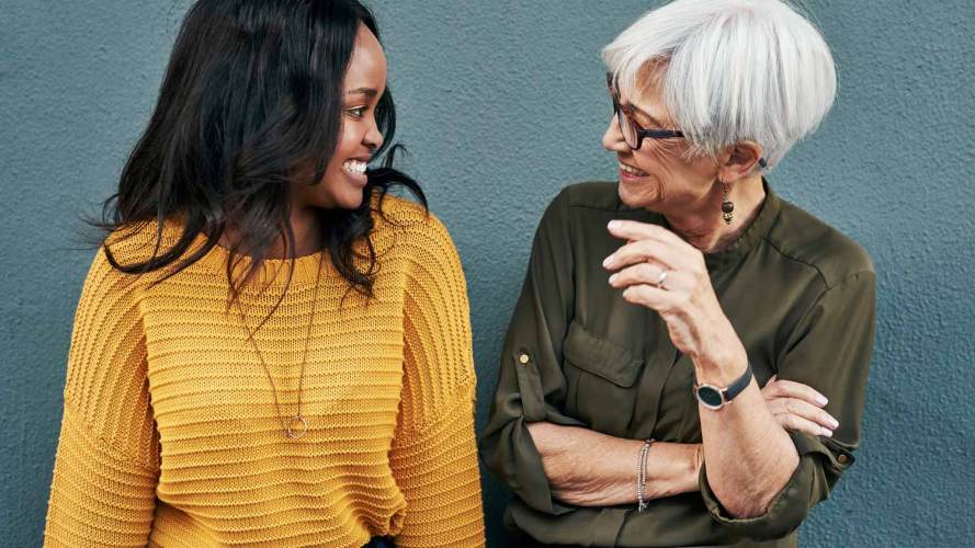 Two female coworkers from different generations chat, part of an intergenerational workforce.