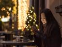 A woman sits outside a cafe using her phone for a retail shopping experience