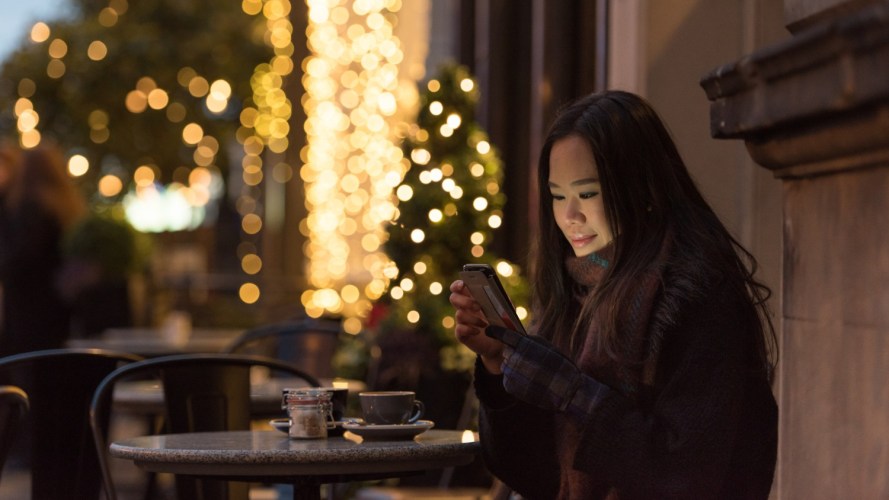 A woman sits outside a cafe using her phone, a retail shopping experience