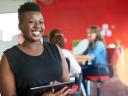 Casual portrait of an african american business woman using technology in a bright and sunny startup with the team in the background