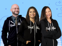 A group of three Developer Trailblazers stand together in their black Trailblazer hoodies against a blue background with line art details.