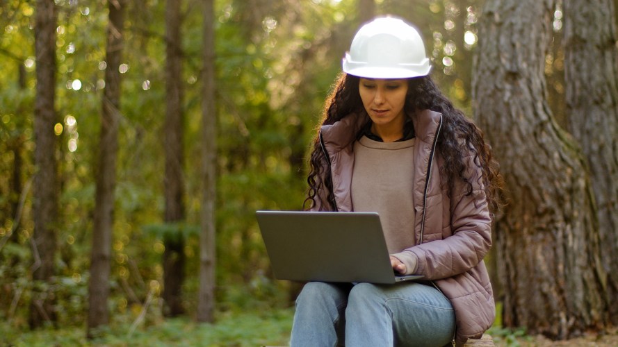 woman-sitting-in-woods-wearing-hard-hat-with-computer