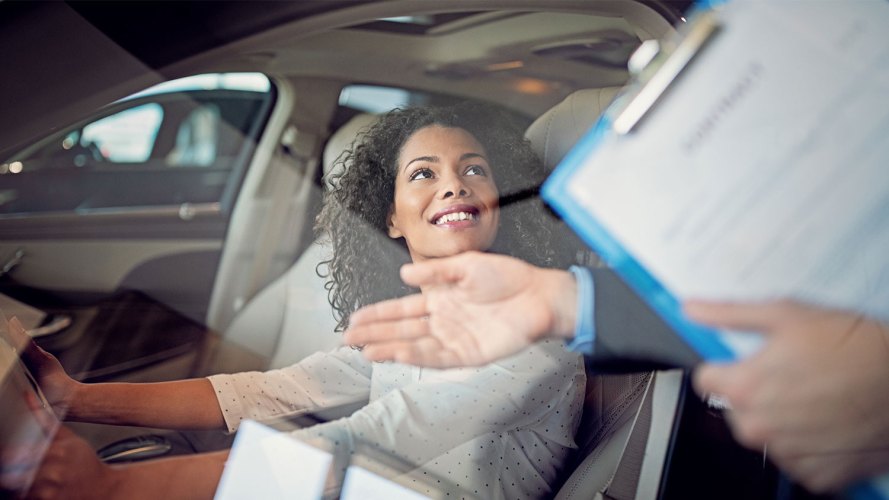 A woman sits behind the wheel of a car at a dealership: trends in automotive