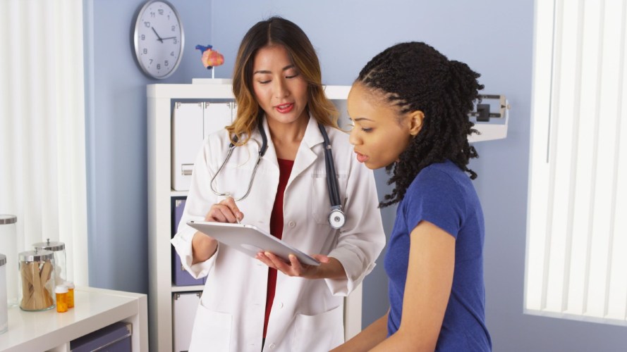 A woman in a white lab coat discusses the healthcare platform data seen on a tablet with a patient.