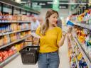 A woman reads the label of a food package in the aisle of a grocery store, a common consumer behavior.