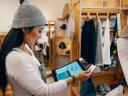 Retail shop clerk viewing consumer goods industry trends on a digital tablet in her store.